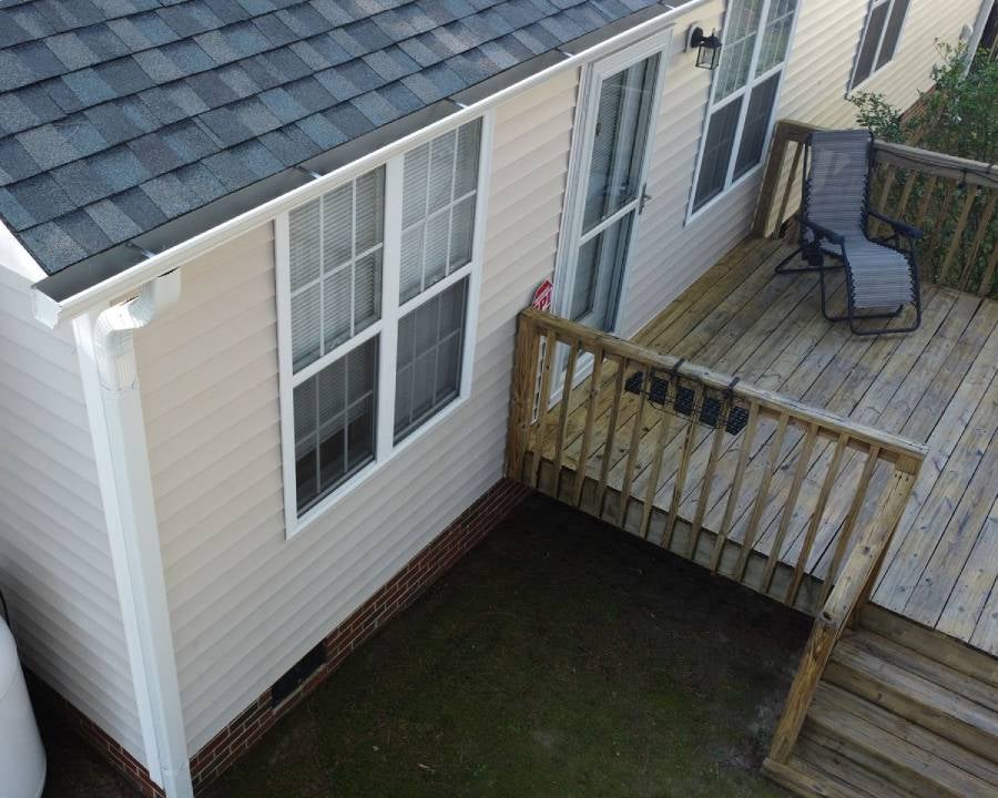 Overhead view of a house with light siding, dark roof, white gutters, and a wooden deck with a lounge chair.
