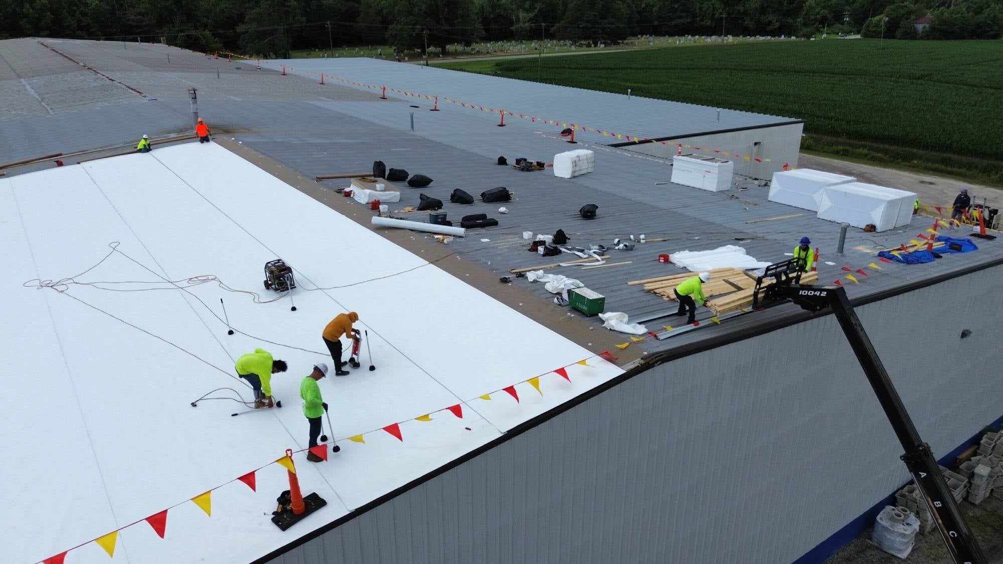 Roofers installing a new white membrane roof on a large commercial building, with safety flags lining the edge.