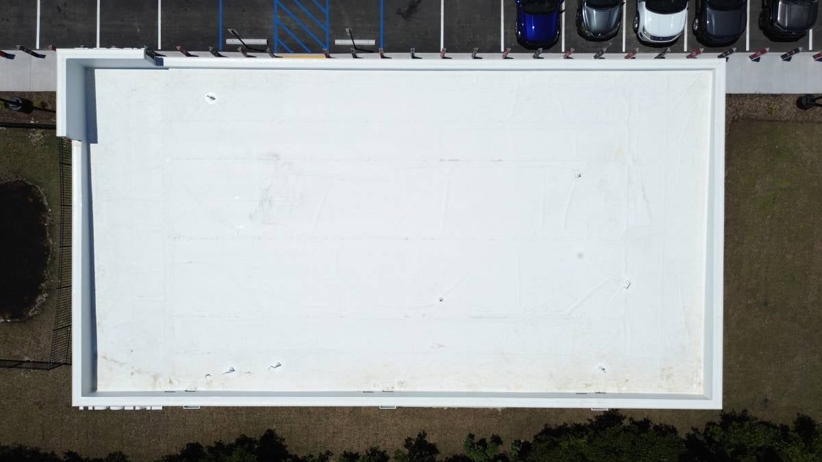 Aerial view of a large, flat white roof, with a parking lot and a few cars on one side.