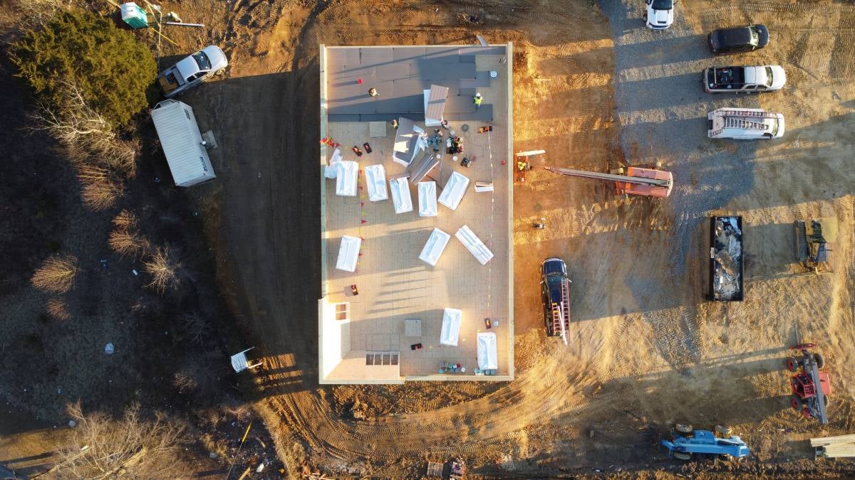 Aerial view of a rectangular building under construction, surrounded by construction vehicles, equipment, and dirt.
