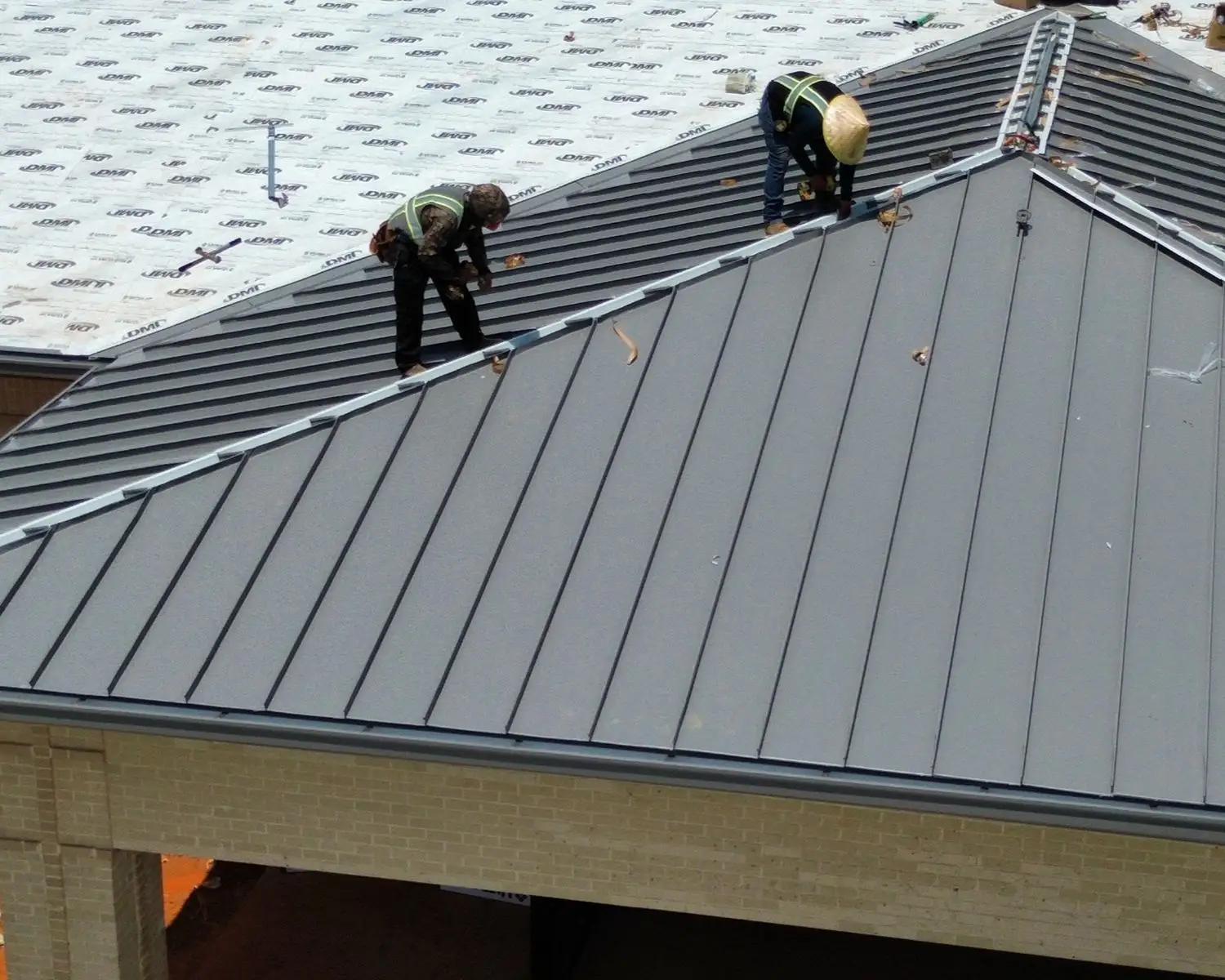 Two roofers install dark gray metal panels on a new roof.