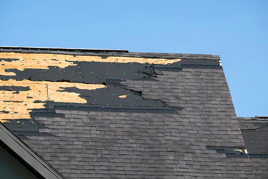 A roofer in a hard hat and safety vest seals brown tile roof with a caulking gun.